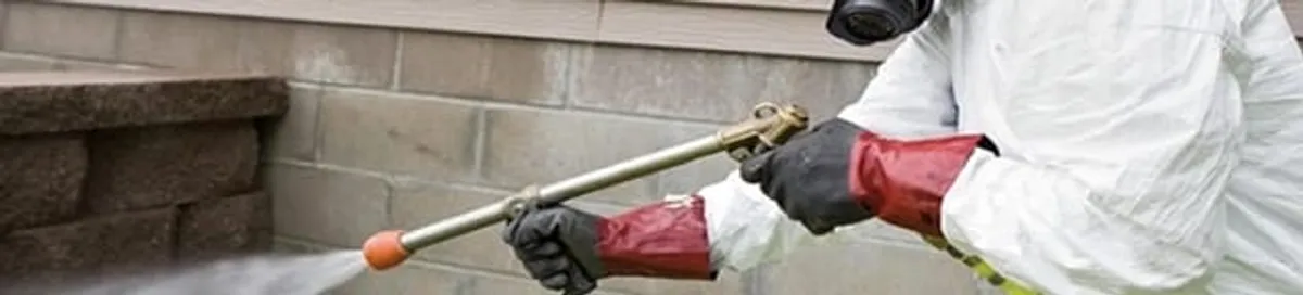 Pest control technician applying exterior insect treatment along a home foundation in Shreveport, LA