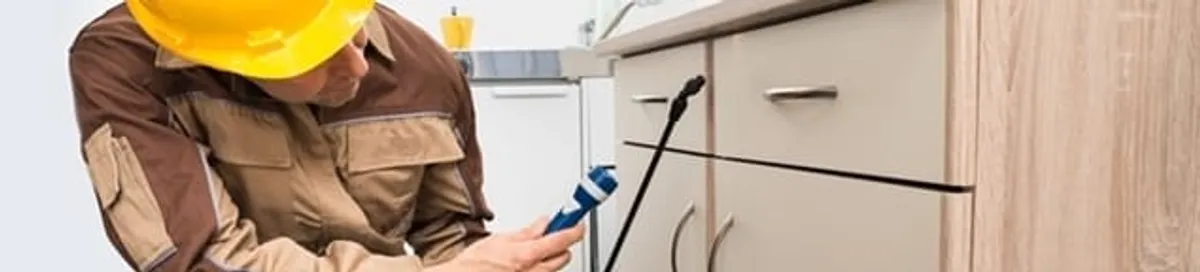 Roach exterminator applying treatment under kitchen cabinets in Shreveport, LA