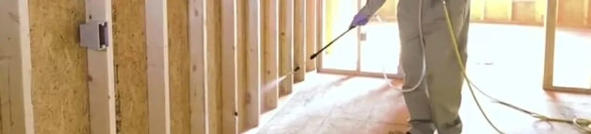 Termite treatment technician applying spray along framing and unfinished walls in Shreveport, LA